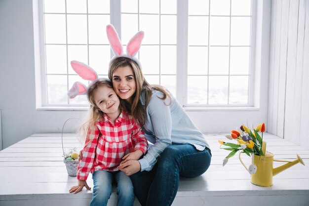 Ragazza e madre nelle orecchie del coniglietto che si siedono vicino al canestro con le uova di Pasqua