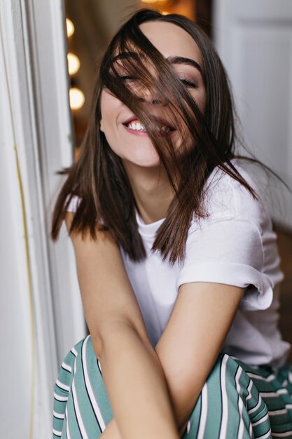 Ragazza eccitata con capelli castani lisci che ridono alla macchina fotografica al mattino Modello femminile gioioso con pelle leggermente abbronzata che esprime felicità