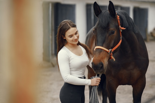 Ragazza elegante in una fattoria con un cavallo