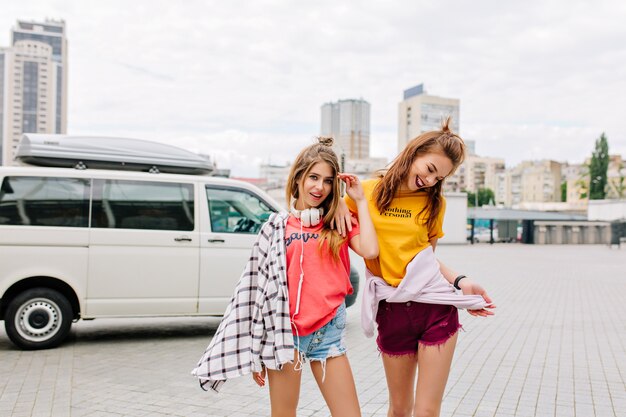 Ragazza emozionante con capelli castani che balla in shorts in denim e guarda con sorriso