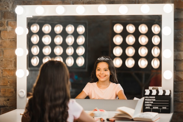 Ragazza felice che esamina la sua riflessione in specchio al backstage