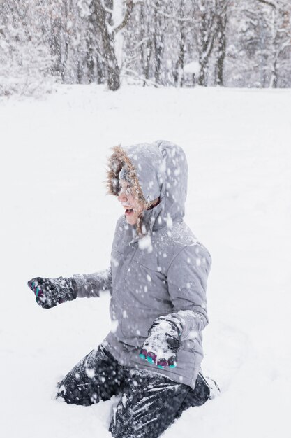 Ragazza felice che gode delle precipitazioni nevose alla foresta in inverno