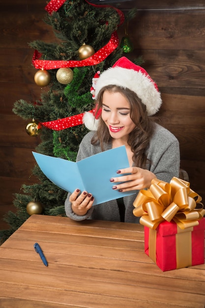 Ragazza felice che legge le congratulazioni di Capodanno e Natale dal suo ragazzo che le ha inviato una scatola di regali di colore rosso