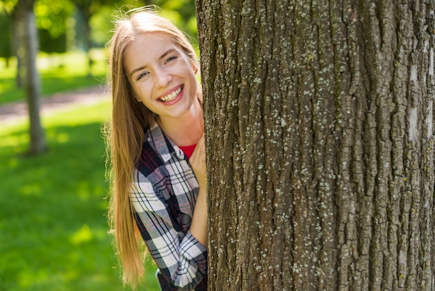 Ragazza felice che propone dietro un albero