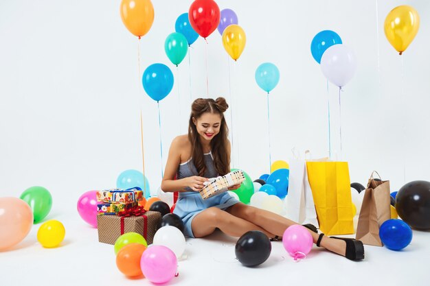 Ragazza felice che scopre le scatole del regalo di compleanno che si siedono con i palloni dell'elio