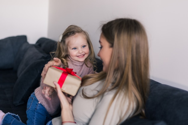 Ragazza felice che sorprende sua madre con il regalo a casa in salone