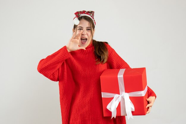 ragazza felice con cappello santa tenendo presente chiamando qualcuno in piedi su bianco