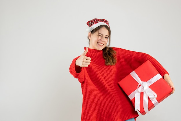 ragazza felice con il cappello della Santa che fa il pollice sul regalo della tenuta del segno su bianco