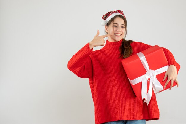 ragazza felice con il cappello della santa che indica con più fine il suo regalo della tenuta del sorriso su bianco