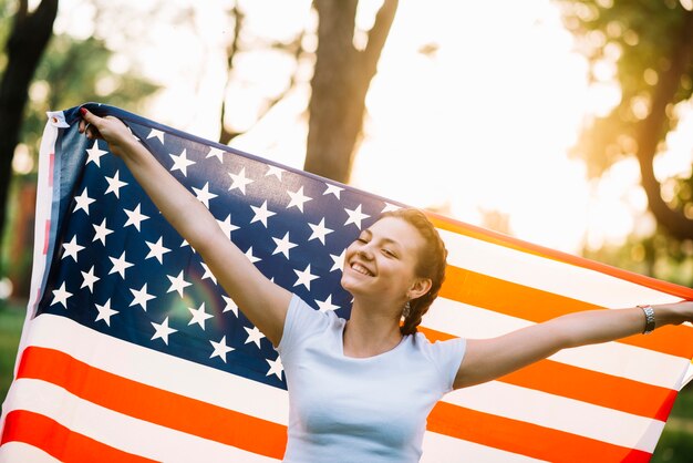 Ragazza felice con la bandiera americana in natura