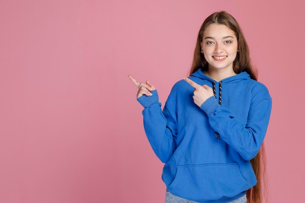 Ragazza felice con lunghi capelli biondi che puntano lontano con le dita che mostrano la giusta direzione e sorridente