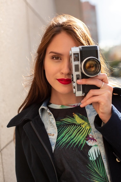 Ragazza felice dei pantaloni a vita bassa che fa foto con la retro macchina fotografica sulla via della città. Concetto di viaggio