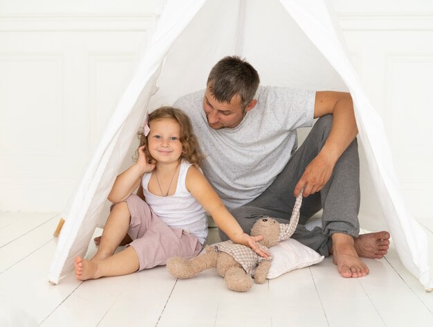 Ragazza felice della foto a figura intera che si siede con suo padre