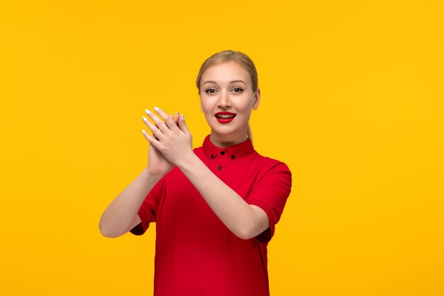 Ragazza felice di giorno della camicia rossa che batte le mani in una camicia rossa su una priorità bassa gialla