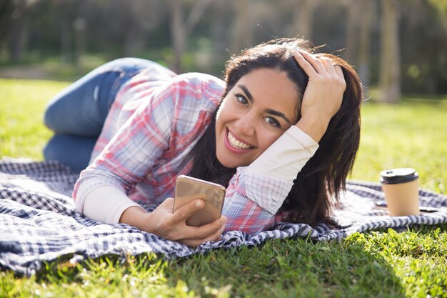 Ragazza felice eccitata dello studente che riposa nel parco e che invia i messaggi