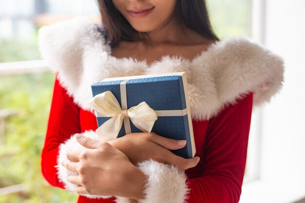 Ragazza felice in costume di Natale che abbraccia scatola regalo blu