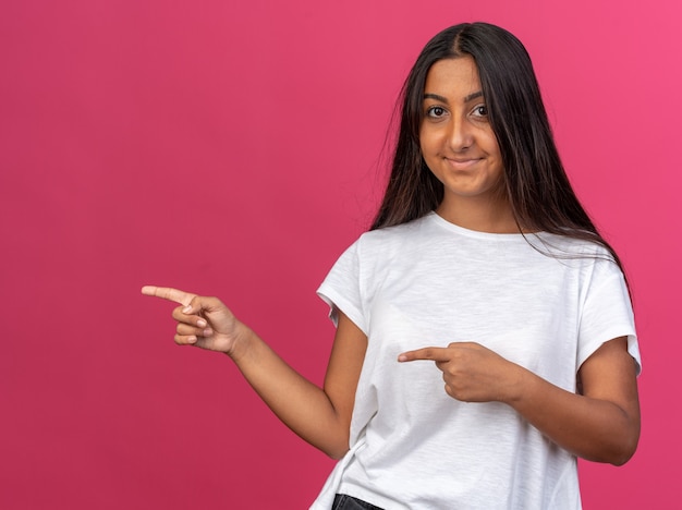 Ragazza felice in maglietta bianca che guarda l'obbiettivo sorridente che punta con le dita indice al lato