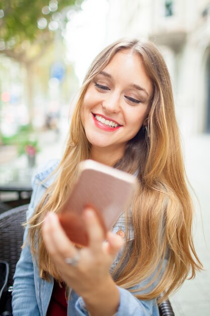 Ragazza felice spensierata dello studente che smsing sullo smartphone