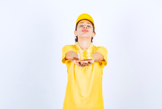 Ragazza femminile in uniforme gialla che consegna una tazza di noodle da asporto gialla al cliente.