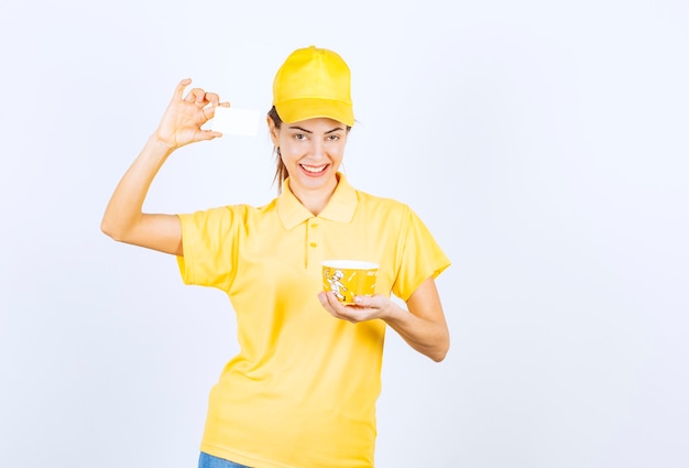 Ragazza femminile in uniforme gialla che consegna una tazza di noodle da asporto gialla e presenta il suo biglietto da visita al cliente.