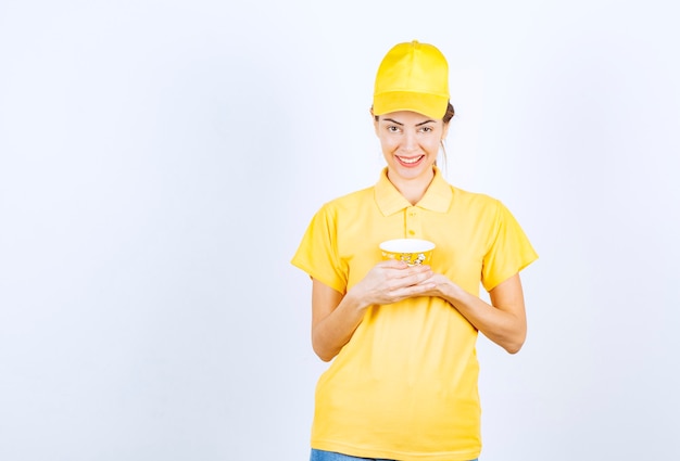 Ragazza femminile in uniforme gialla che tiene una tazza di noodle da asporto gialla.