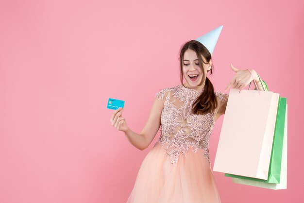 ragazza festaiola con tappo di partito che tiene carta e borse della spesa sul rosa