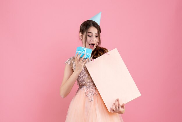 ragazza festaiola con tappo di partito che tiene regalo e borsa della spesa sul rosa