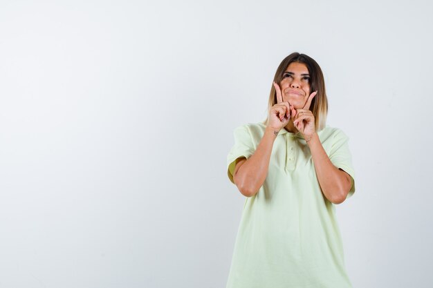 Ragazza giovane appoggiando il mento sulla mano, rivolto verso l'alto, guardando verso l'alto in t-shirt e guardando allegra, vista frontale.