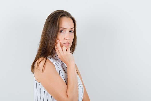 Ragazza giovane con due dita sulla guancia in maglietta e guardando pensieroso. .