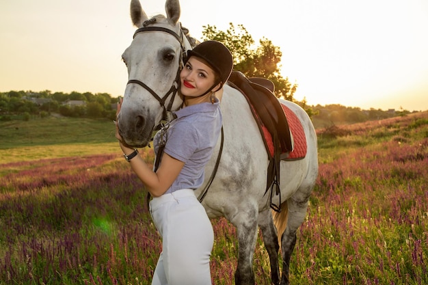 Ragazza giovane fantino che accarezza e abbraccia il cavallo bianco nel tramonto di sera