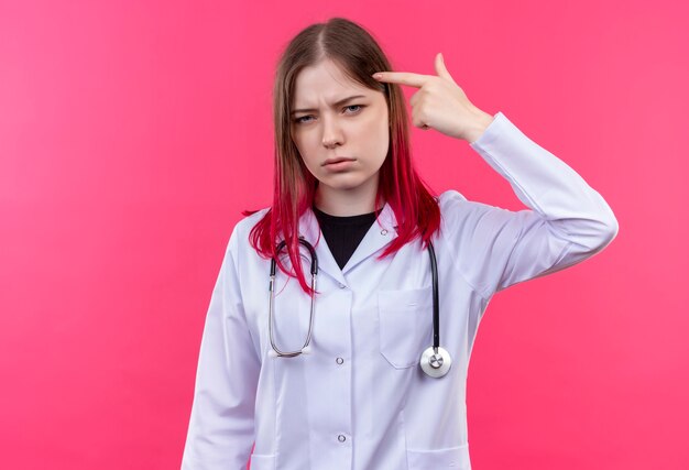 Ragazza giovane medico che indossa abito medico stetoscopio - sulla parete isolata rosa