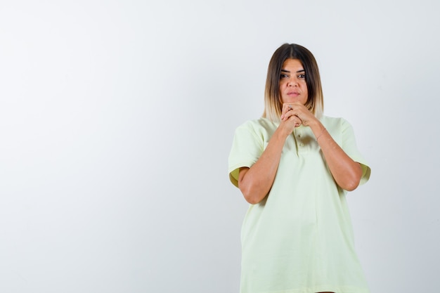 Ragazza giovane stringendo le mani sotto il mento in maglietta e guardando seria. vista frontale.