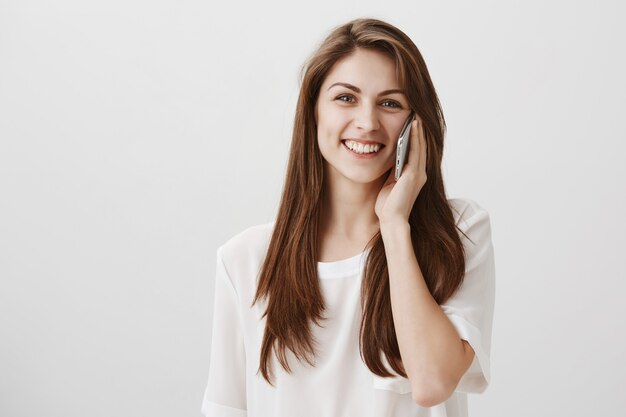 Ragazza graziosa allegra che comunica sul telefono e sul sorridere