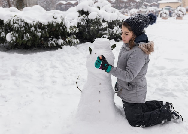 Ragazza graziosa che fa pupazzo di neve durante la stagione invernale