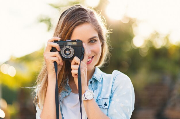 Ragazza graziosa che prende le foto con una macchina fotografica d'annata un giorno soleggiato