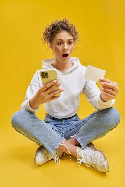 Ragazza graziosa che si siede sulle gambe che tengono smatphone e carta