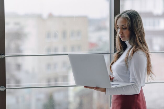 Ragazza graziosa con un computer portatile dalla finestra