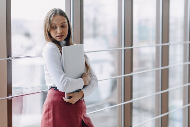 Ragazza graziosa con un computer portatile dalla finestra