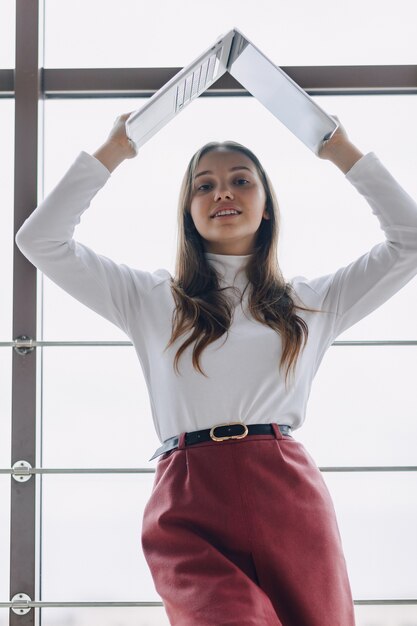 Ragazza graziosa con un computer portatile dalla finestra