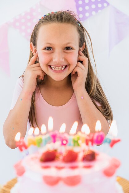 Ragazza graziosa sorridente che sta vicino alla torta di compleanno