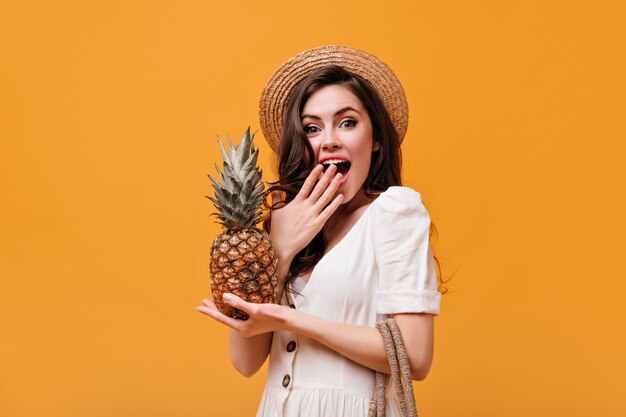 Ragazza in abito bianco e alle imbarcazioni si copre la bocca per la sorpresa e tiene l'ananas.