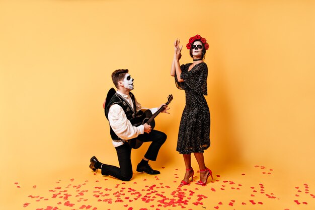 Ragazza in abito elegante con rose tra i capelli sta ballando la danza spagnola al suono della chitarra. Il giovane si leva in piedi su un ginocchio e canta una canzone alla sua amata donna