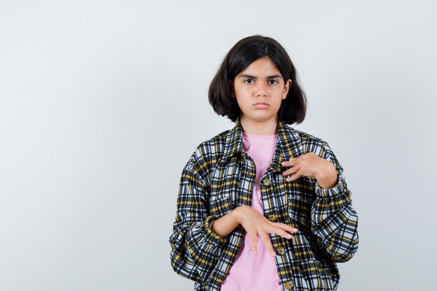 Ragazza in camicia a quadri e t-shirt rosa che indica se stessa con le mani e sembra seria