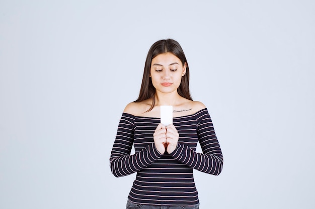 Ragazza in camicia a righe che presenta il suo biglietto da visita con fiducia.