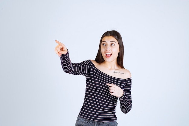 Ragazza in camicia a righe che punta a qualcuno sul lato sinistro.