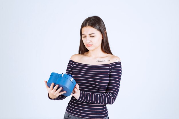 Ragazza in camicia a righe che tiene una scatola regalo a forma di cuore blu e si entusiasma.