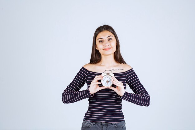 Ragazza in camicia a righe che tiene una sveglia e la promuove come un nuovo prodotto.