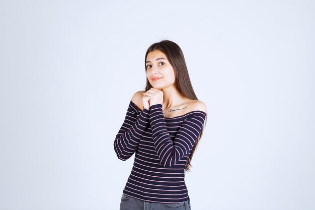 Ragazza in camicia a righe che unisce le sue mani e che prega.