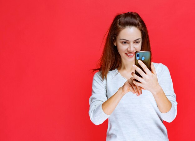 Ragazza in camicia bianca che tiene in mano un nuovo modello di smartphone e fa una videochiamata o si fa un selfie