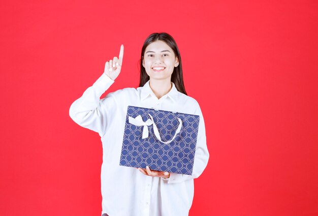 Ragazza in camicia bianca con in mano una borsa della spesa blu e sembra confusa e pensierosa